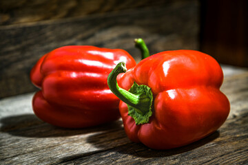 Two red bell peppers lie on a wooden table.