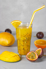 Tropical fresh of mango, passionfruit and orange in tall glass on light gray background