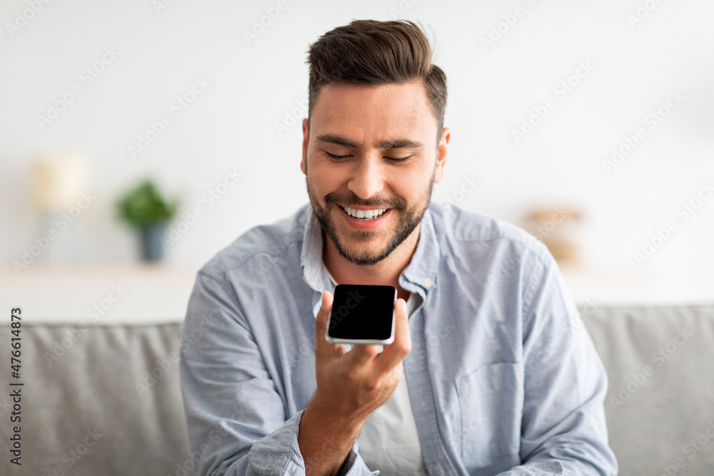 Poster happy handsome man recording voice message on smartphone or using virtual assistant while resting on