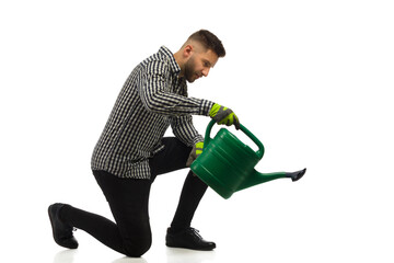 Young kneeling and focused man is watering by using a watering can. - obrazy, fototapety, plakaty