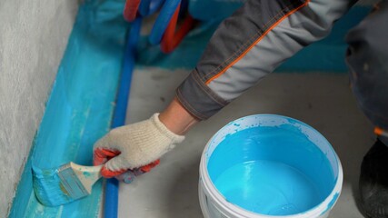 A worker applies waterproofing paint to the bathroom wall and floor. Applying waterproofing in the...