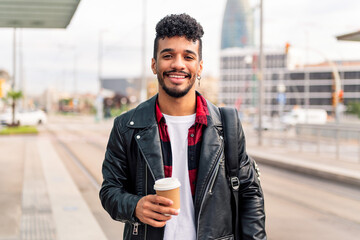 young latin guy smiles with a coffee on his hand