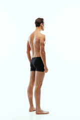 Back view of young handsome shirtless sportive man wearing black boxer-briefs standing isolated on white studio background.