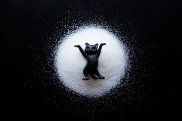 Funny black toy kitten in a circle of white powder. Concept of winter active recreation and...