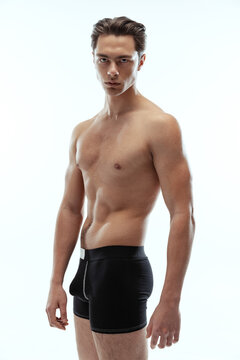 Half-length portrait of young handsome shirtless sportive man wearing black boxer-briefs standing isolated on white background.