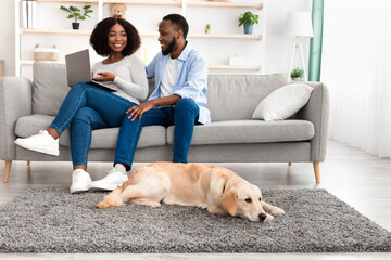 Black couple at home using laptop sitting with dog
