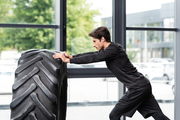 Fototapeta na wymiar Side view of sportsman training with tire in gym