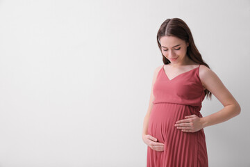 Beautiful young pregnant woman on light background. Space for text