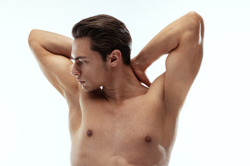 Portrait of young handsome sportive shirtless man standing with crossed arms behind his head isolated on white background.