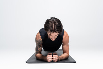 Fototapeta na wymiar Sportsman in sleeveless shirt doing plank on fitness mat on grey background