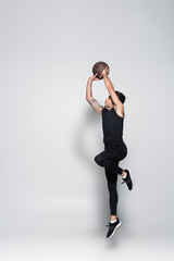 Obraz premium Side view of tattooed sportsman with basketball ball jumping on grey background