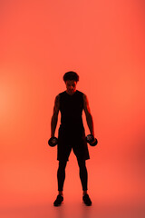 Athletic man in sportswear holding dumbbells on red background