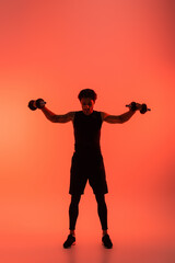 Fototapeta na wymiar Sportsman training with dumbbells on red background