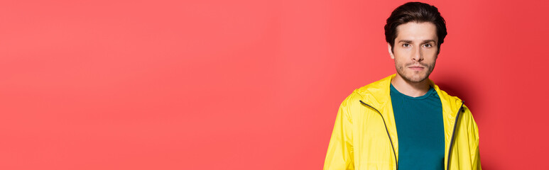 Brunette sportsman in yellow sports jacket looking at camera on red background, banner