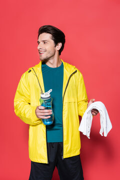 Happy sportsman holding towel and sports bottle on red background