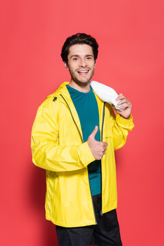 Smiling sportsman in yellow sports jacket showing like and holding towel on red background