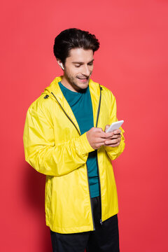 Happy sportsman in earphone using cellphone on red background