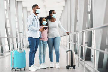 Black family in masks traveling, holding documents in airport
