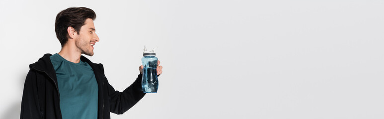 Side view of positive sportsman holding sports bottle on grey background, banner