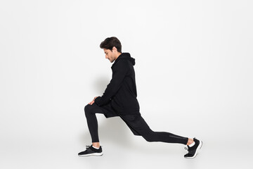 Side view of sportsman in sports jacket doing lunges on grey background
