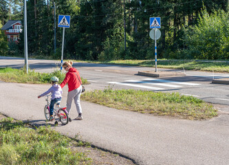 Mom with a child on a bike walk, a woman teaches a child to ride a bike. Walk on the bike path on a summer day
