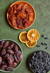 Dried apricots, raisins, dates and slices of dried orange, flat lay on a green background