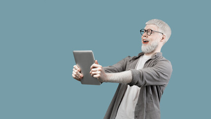 Emotional albino man looking at tablet in surprise, reading unbelievable news, turquoise background with free space