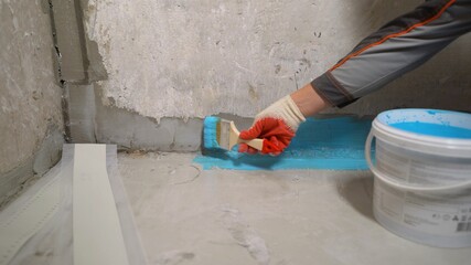 A worker applies waterproofing paint to the bathroom wall and floor. Applying waterproofing in the bathroom. - obrazy, fototapety, plakaty
