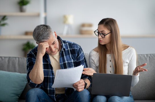 Serious mature couple with laptop checking documents at home. Family budget, marriage contract concept