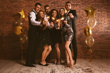 Happy friends with glasses of sparkling wine and sparklers celebrating New Year indoors