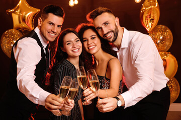 Happy friends with glasses of sparkling wine celebrating New Year indoors