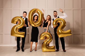 Happy friends with golden 2022 balloons indoors. New Year celebration