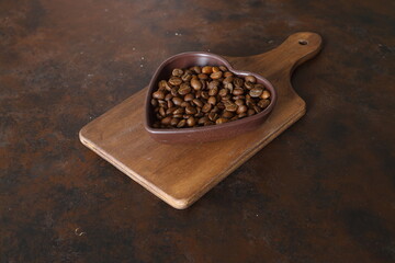 Roasted coffee beans in heart shaped bowl on dark background. Love coffee concept. Top view flat lay with copy space	
