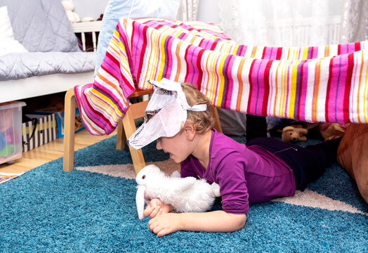 A child in a wolf mask, plays in the children's room. The child built a tent with chairs and bedspreads.
