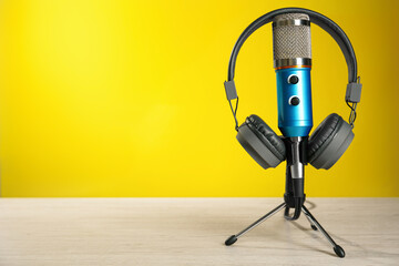 Microphone and modern headphones on white wooden table against yellow background, space for text