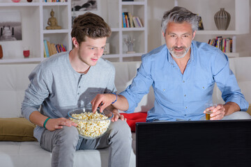 Two men engrossed in the television, eating popcorn