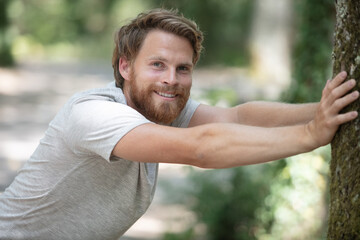 handsome young man leaning against tree pushing it