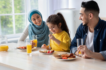Cheerful middle eastern family of three having healthy breakfast together in kitchen