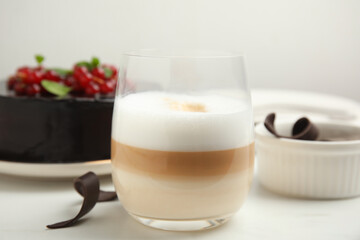 Glass of coffee, delicious cake and chocolate curls on white table