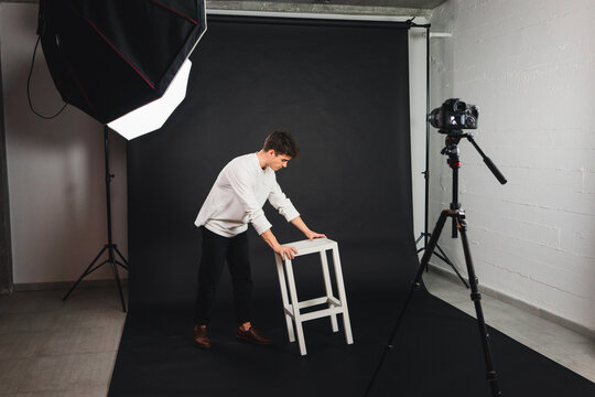 Male carrying chair on black backdrop in studio