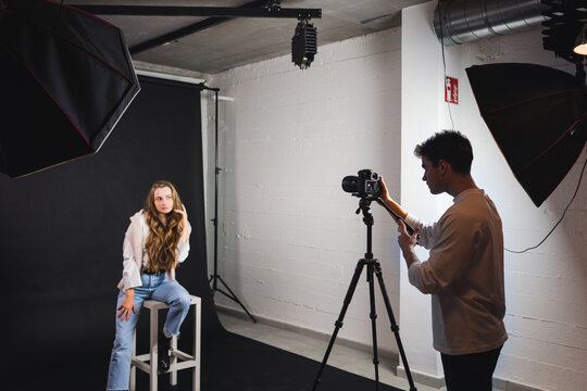 Male taking photo of female sitting on chair in professional studio