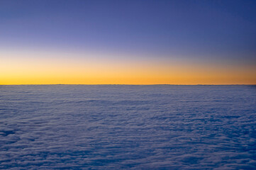 view of the horizon above the clouds at dawn from the inside of the plane