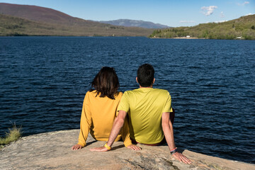 Fototapeta premium Couple sitting together on the rocks in the Sanabria lake at sunset. Zamora, Spain.