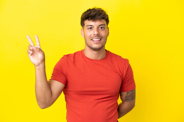 Young caucasian handsome man isolated on yellow background smiling and showing victory sign