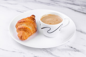 White ceramic plate with Cup of coffee and croissant on marble texture background.