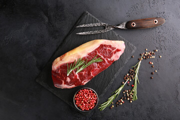 Raw meat. Steak marble beef on a dark board with spices, rosemary, iron fork on a black table. Background image, copy space, flatlay, top view