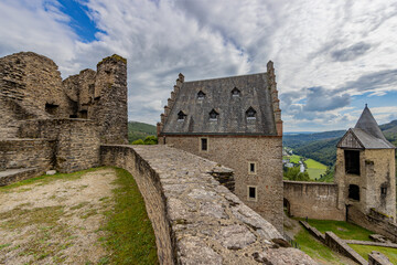 Fototapeta na wymiar Upper courtyard in the outdoor ruins of the medieval castle of Bourscheid, ruined walls, a building and the watchtower, hills covered with lush green trees in the background, Luxembourg