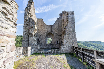Front view of what was a tower with a window, destroyed and damaged stone walls in Brandenburg castle, hills with green trees in the background, sunny summer day with clear blue sky in Luxembourg