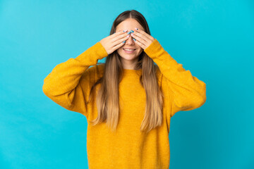 Young Lithuanian woman isolated on blue background covering eyes by hands and smiling