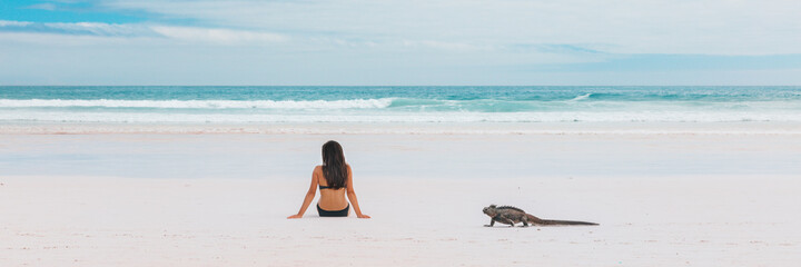 Beach vacation funny marine iguana walking by woman tanning on Galapagos islands travel banner....